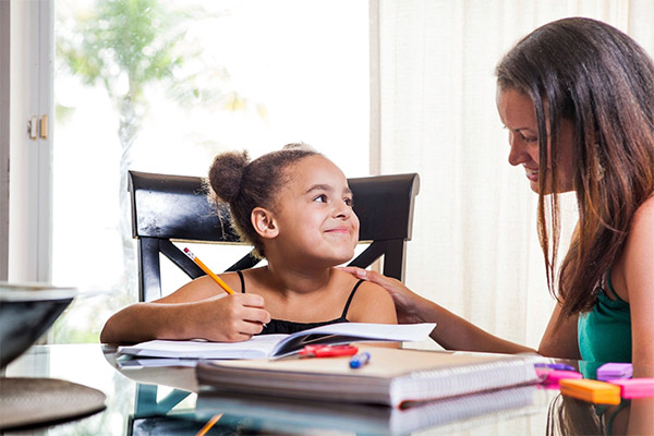 A woman and girl sitting at table with papers.