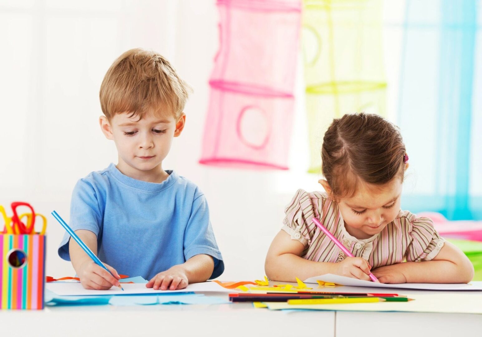 Two children are sitting at a table and writing.