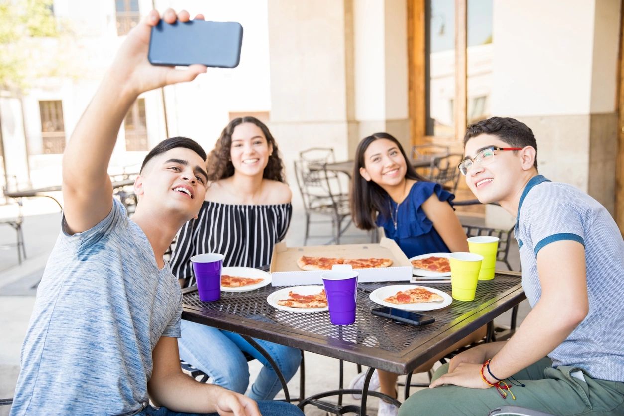 A group of people sitting at a table taking a picture with their cell phone.