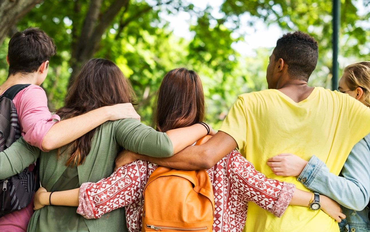 Three women are hugging each other in a park.